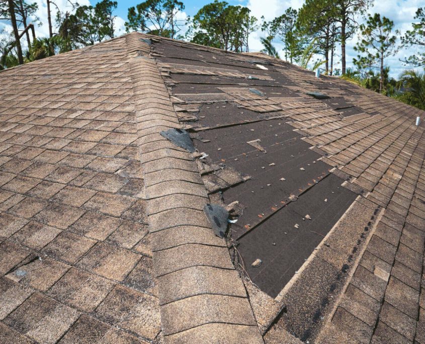 A roof with several missing shingles, indicating potential wind damage A roof with several missing shingles after wind damage