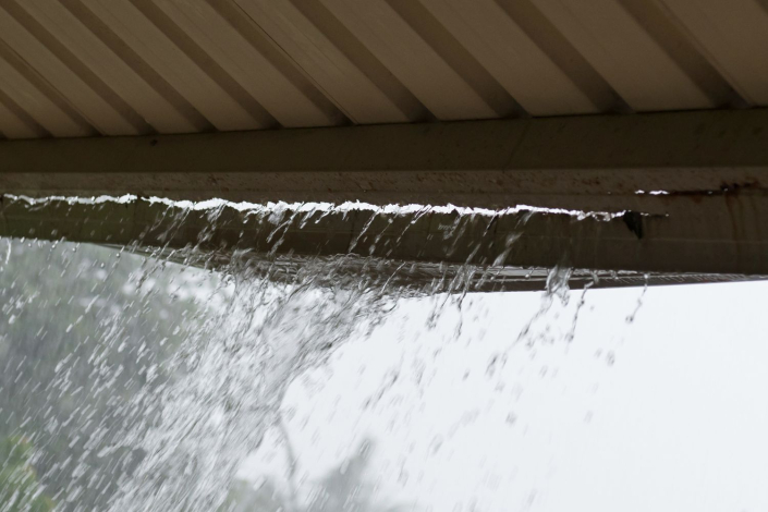 Residential gutter is overflowing due to debris and damage.