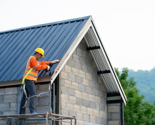 A construction worker in an orange vest and hard hat is actively working on a residential building.