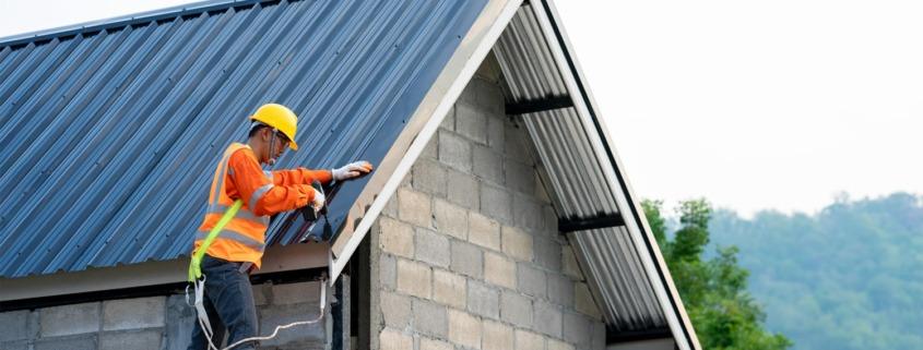 A construction worker in an orange vest and hard hat is actively working on a residential building.