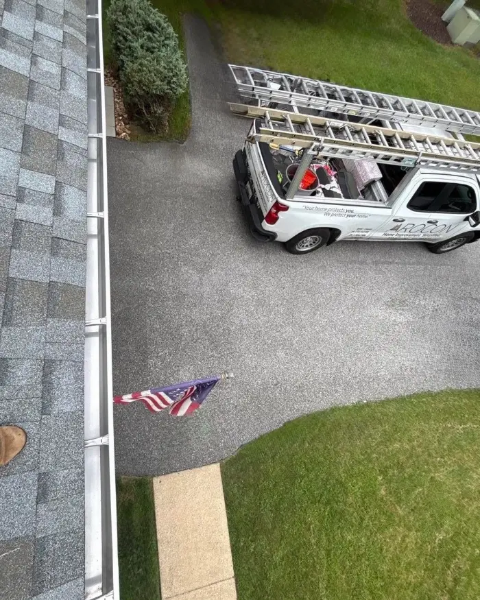 View from the roof edge: a clean gutter and the AROCON truck with ladders parked in the driveway