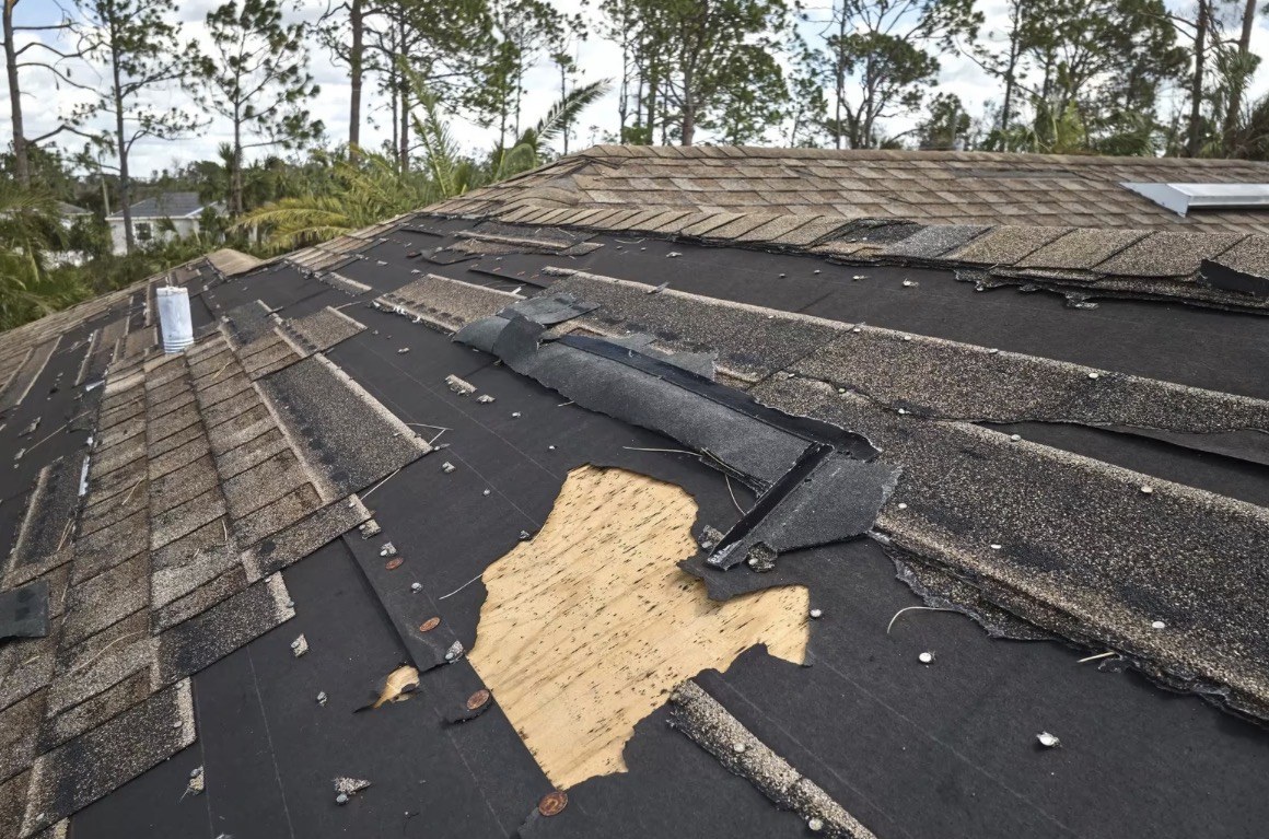 Roof with wind-torn shingles and exposed decking after a storm